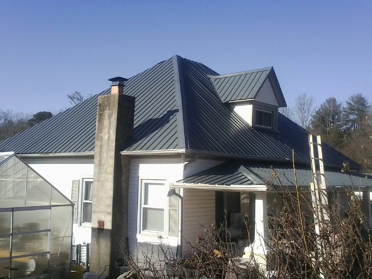 Dark blue standing seam metal roof on a white farmhouse with dormer — Slate & Tile Roof Repair by Roofing Brothers in Beccaria