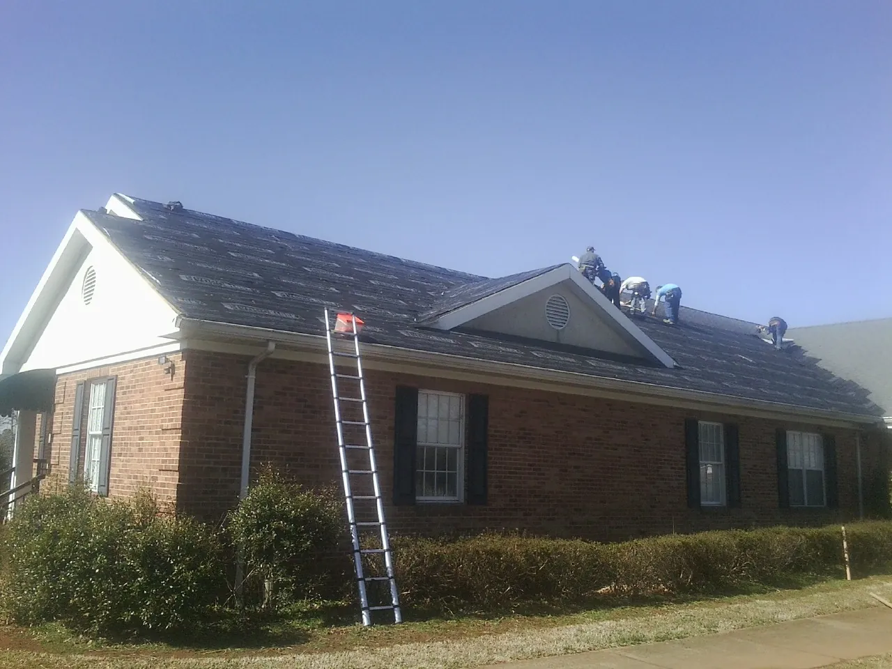 Crew tearing shingles off a brick ranch roof with a ladder set — Metal Roof Repair work by our crew in Beccaria