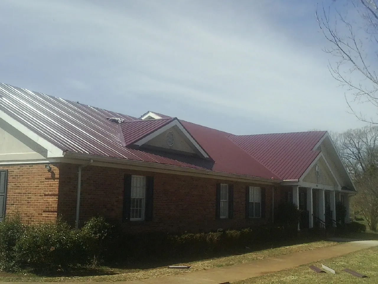 Red metal roof with gabled entries on a long brick building, from a Hail Damage Roof Repair job in Beccaria
