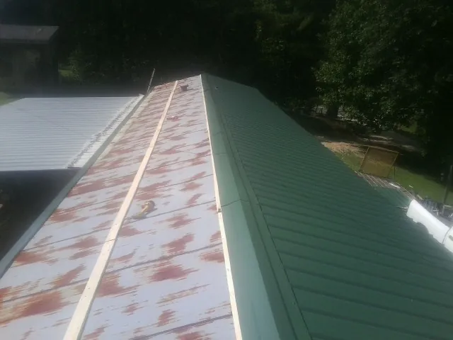 Old rusted panels beside newly installed green metal roofing — Wind Damage Roof Repair by Roofing Brothers in Beccaria