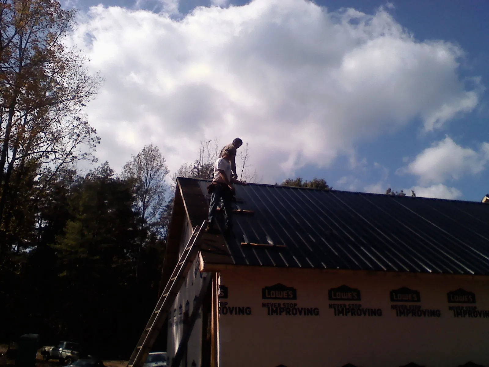 Roofer fastening dark metal panels high against a cloudy sky, from a Roof Inspection job in Beccaria