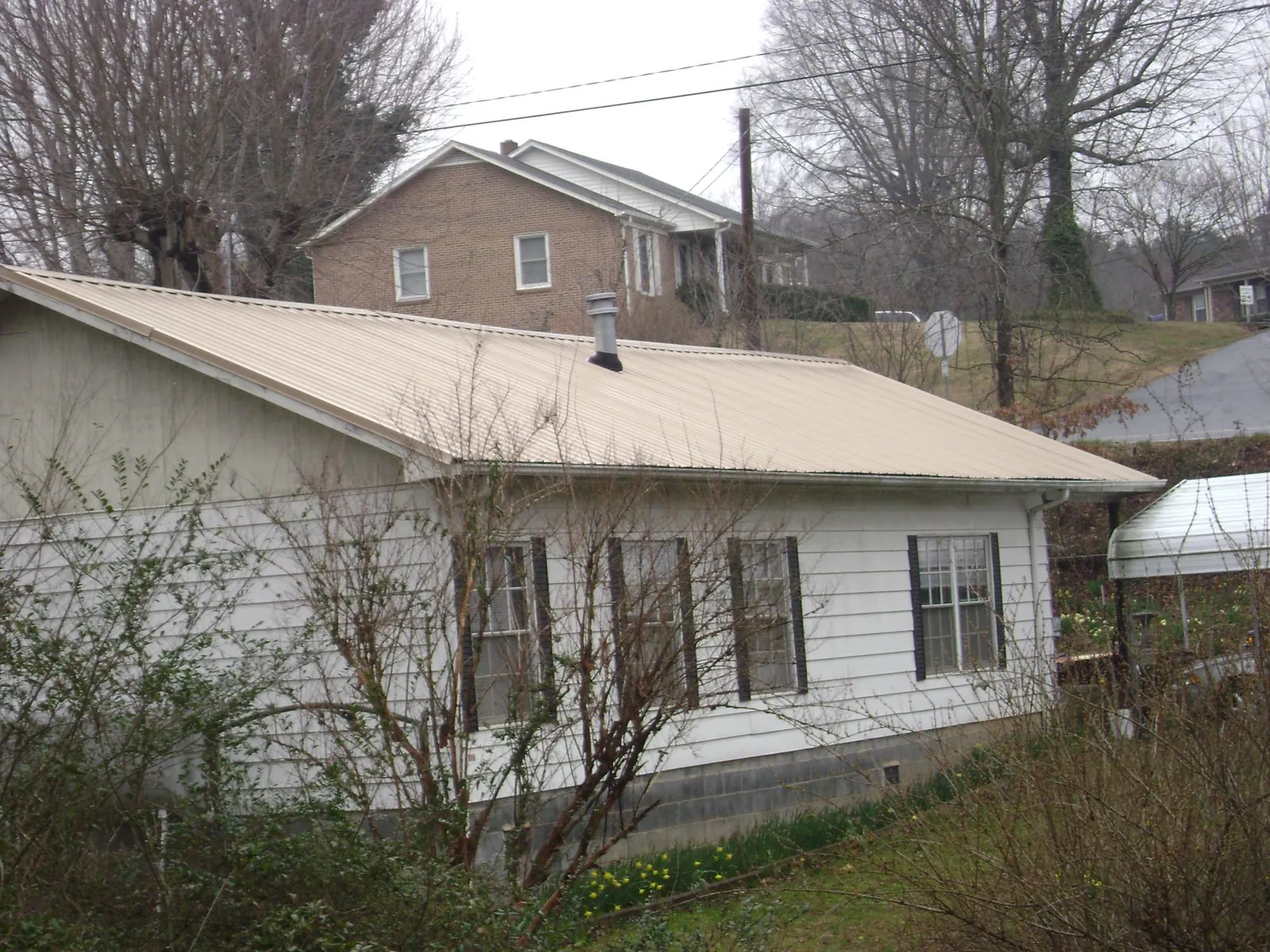 Tan metal roof on a white sided house set into a hillside — Commercial Roofing by Roofing Brothers in Beccaria