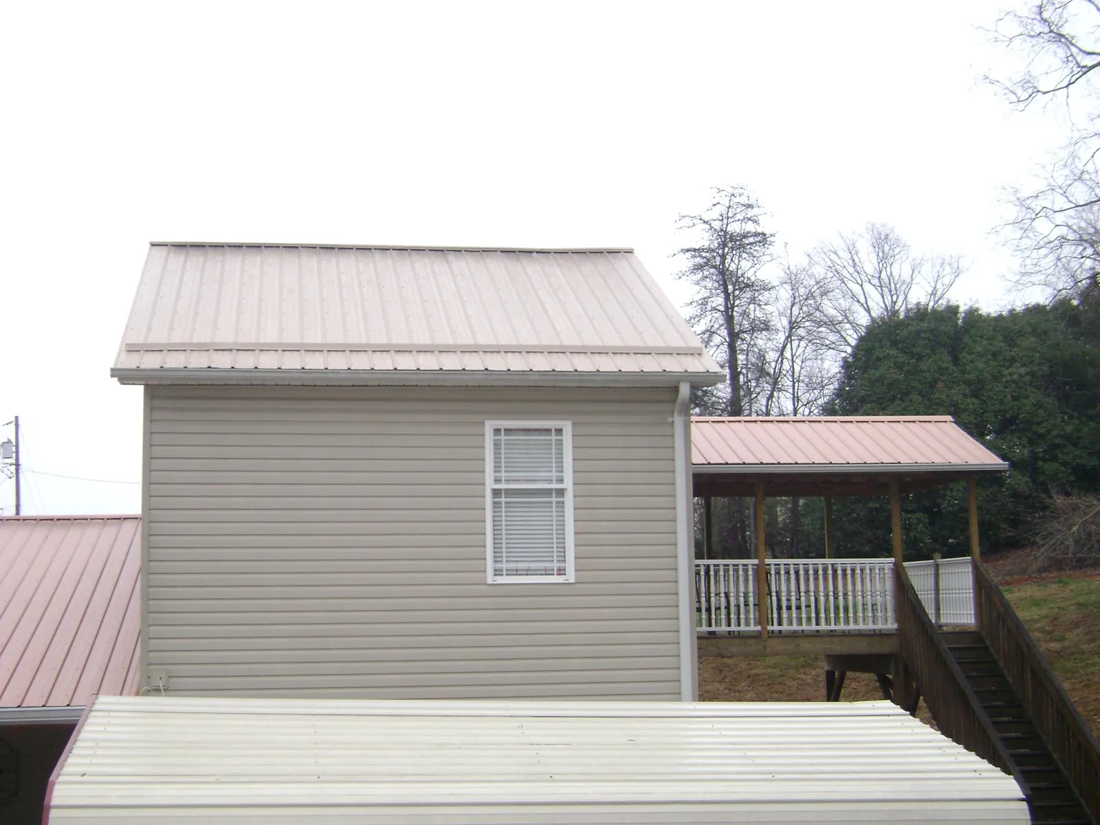 Tan metal roofs on a two story addition and attached porch, from a Roof Replacement job in Beccaria